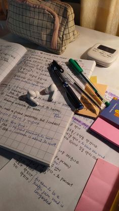 an open notebook sitting on top of a table next to pens and paper with writing