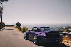 a purple car parked on the side of a road next to some trees and bushes