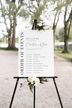 a welcome sign with flowers on it in the middle of a park setting for an outdoor ceremony