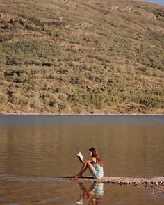 a woman sitting in the water reading a book