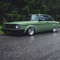 a green car is parked on the side of the road in front of some trees