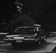 an old black and white photo of a car on the road with trees in the background