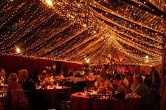 people are sitting at tables in a large room with lights on the walls and ceiling