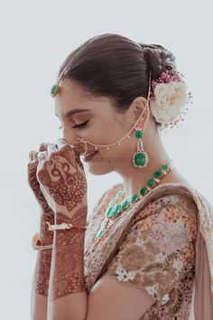 a woman with henna and jewelry on her hand holding a flower in front of her face