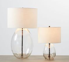 two clear glass lamps on a table with a white linen lamp shade and a gold metal base