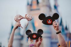 two people holding mickey mouse ears in front of a castle