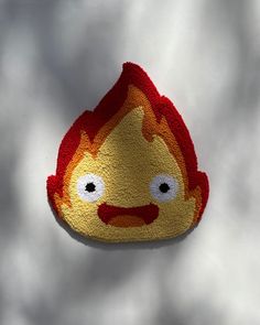 a red and yellow fire emo brooch on a white surface with clouds in the background