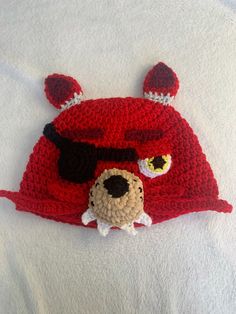 a crocheted red hat with ears and eyes on top of a white blanket