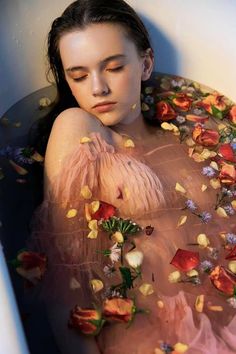 a woman in a bathtub with flowers all over her body and head, surrounded by petals