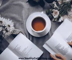 two open books on a table with flowers and a cup of tea next to them