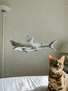 a cat sitting on top of a bed next to a light fixture that looks like a shark