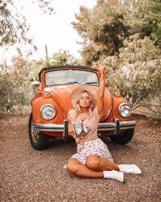 a woman sitting on the ground next to an orange car with her arms in the air