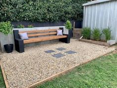 a wooden bench sitting on top of a gravel covered ground next to a garden area