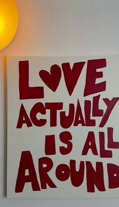 a red and white sign that says love actually is all around on the wall next to a lamp