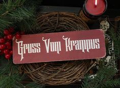 a wooden sign sitting on top of a wreath next to a candle and some berries