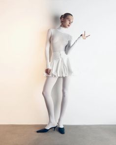 a woman in white is posing with her hand on her hip while wearing tights and heels