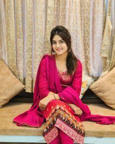 a woman sitting on top of a wooden bench wearing a pink dress and red shoes