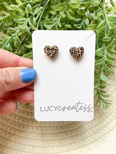 a pair of leopard print heart shaped studs on a white card next to some green plants