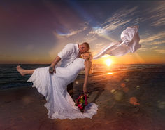 a bride and groom kissing on the beach at sunset with their wedding dress blowing in the wind