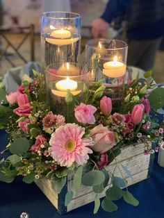 flowers and candles are placed in a wooden box on a blue tablecloth with silverware