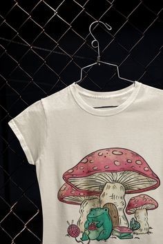 Trendy handmade design with frog knitting in front of mushrooms printed on a tee shirt. Our tees are made 100% of the cleanest, most durable and softest form of cotton. You're going to love this t-shirt and our customer service! Our tees are truly one-of-a-kind, so don't miss out on this unbelievable opportunity! ✈️ SHIPPING AND DELIVERY ✈️ The shipping is totally FREE and thanks to our Automated Processing System we can offer you 1-5 business day delivery times anywhere in the US.  ▪️ Multiple Summer Graphic Tee With Mushroom Print, White Short Sleeve T-shirt With Mushroom Design, White Short Sleeve Tops With Mushroom Print, White Short Sleeve Top With Mushroom Print, White Mushroom Print Short Sleeve Top, Cotton Graphic Tee With Mushroom Design, White Cotton T-shirt With Mushroom Design, White Short Sleeve Tops With Mushroom Design, Relaxed Fit Tops With Mushroom Print For Streetwear