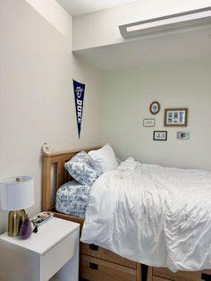 a bed with white sheets and pillows in a bedroom next to a dresser under a window