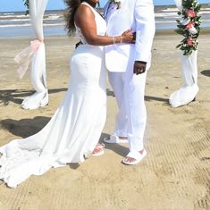 a man and woman standing on top of a sandy beach