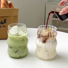 a person pours red wine into two small jars on a table with bread in the background