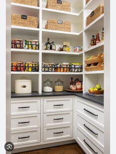 an organized pantry with white cabinets and black counter tops, baskets on the shelves above