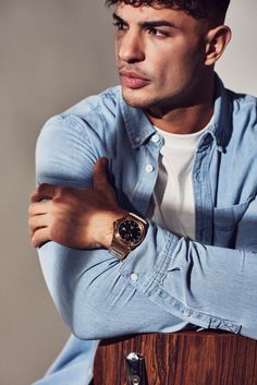 a young man with his arms crossed wearing a blue shirt and watch on his wrist