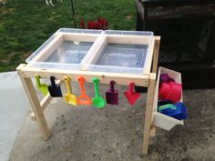 an outdoor play table with plastic utensils and sand trays on it's sides