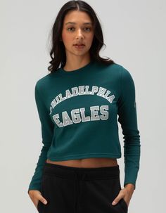 a woman wearing a green philadelphia eagles crop top and black sweatpants is standing in front of a white background