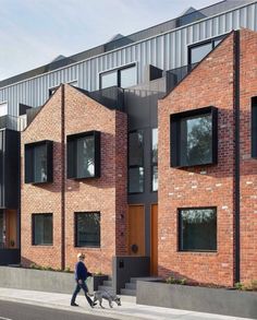 two people walking their dog down the street in front of some brick buildings with windows