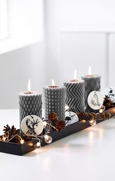 the candles are decorated with pine cones and other holiday decorations on a long black tray