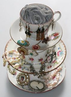 a stack of tea cups and saucers with jewelry on them