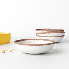 three white bowls with brown rims next to a yellow box