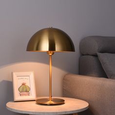 a table with a lamp on it next to a chair and a framed photograph in front of the light