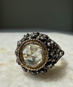 This rose cut diamond antique ring is definitely one of a kind. The silver and 18k yellow gold setting is an original antique. The center rose cut diamond could have been recut/repolished at some point, but sits perfectly in its antique home.  The center diamond is a GIA certified 0.96ct, S-T color, and VS1 clarity stone with strong fluorescence. In certain lighting it appears to be light yellow/champagne in color and really sparkles a ton of warmth, but then in other lighting it takes on a white face-up color due to the fluorescence. The 18k yellow gold bezel  hugs the center rose cut perfectly. It really compliments the stone's beauty. There are very small rose cut slivers set in silver surrounding the open back center stone to give it a pierced dome appearance. The shoulders feature a p Yellow Champagne, Antique Home, Antique Diamond Rings, Antique Ring, Yellow Gold Setting, Small Rose, White Face, Rose Cut Diamond, Antique Rings