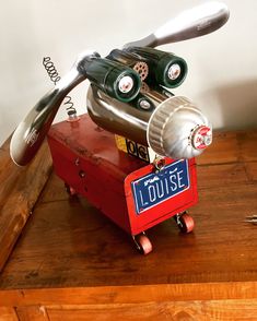 a metal object sitting on top of a wooden table next to a red box with scissors