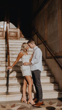 a man and woman standing in front of some stairs with their hands on each other