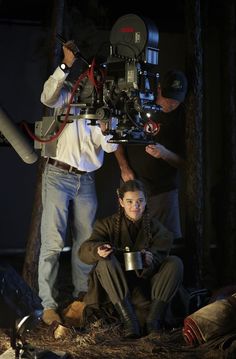 two men are setting up a camera in the woods with another man standing behind them