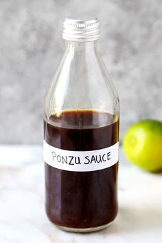 a glass bottle filled with sauce next to an apple