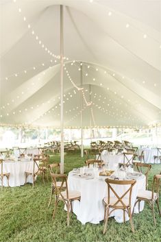 an outdoor tent with tables and chairs set up for a wedding reception under string lights