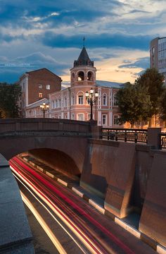 the light streaks are streaking across the street in front of an old building with a clock tower