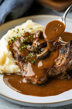 a plate with mashed potatoes, gravy and meat on it is being drizzled by a fork