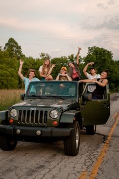 a group of people riding in the back of a green jeep down a road with their arms up