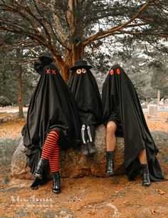 two people in black cloths sitting on a rock with their faces covered by fake eyes