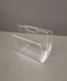 a clear acrylic business card holder on a gray surface with two gold - plated handles