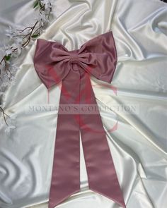 a close up of a pink bow on a white satin bed sheet with flowers in the background