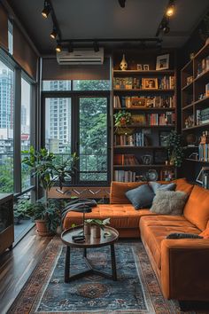 a living room with an orange couch and bookshelf in front of large windows